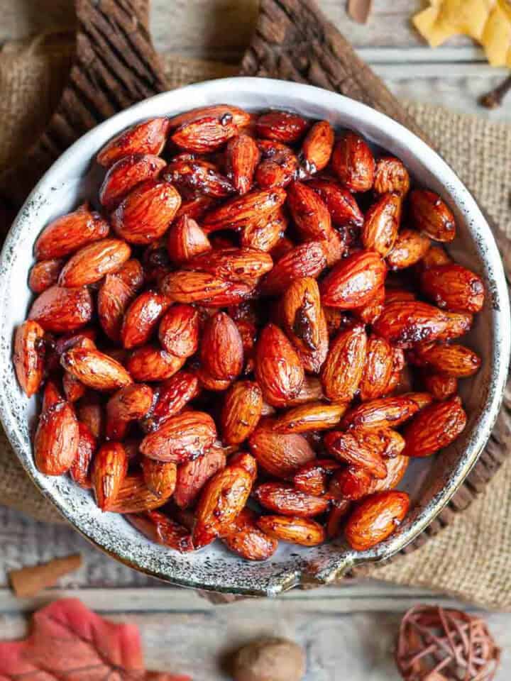 A bowl of roasted almonds on a wooden board with ingredients around.
