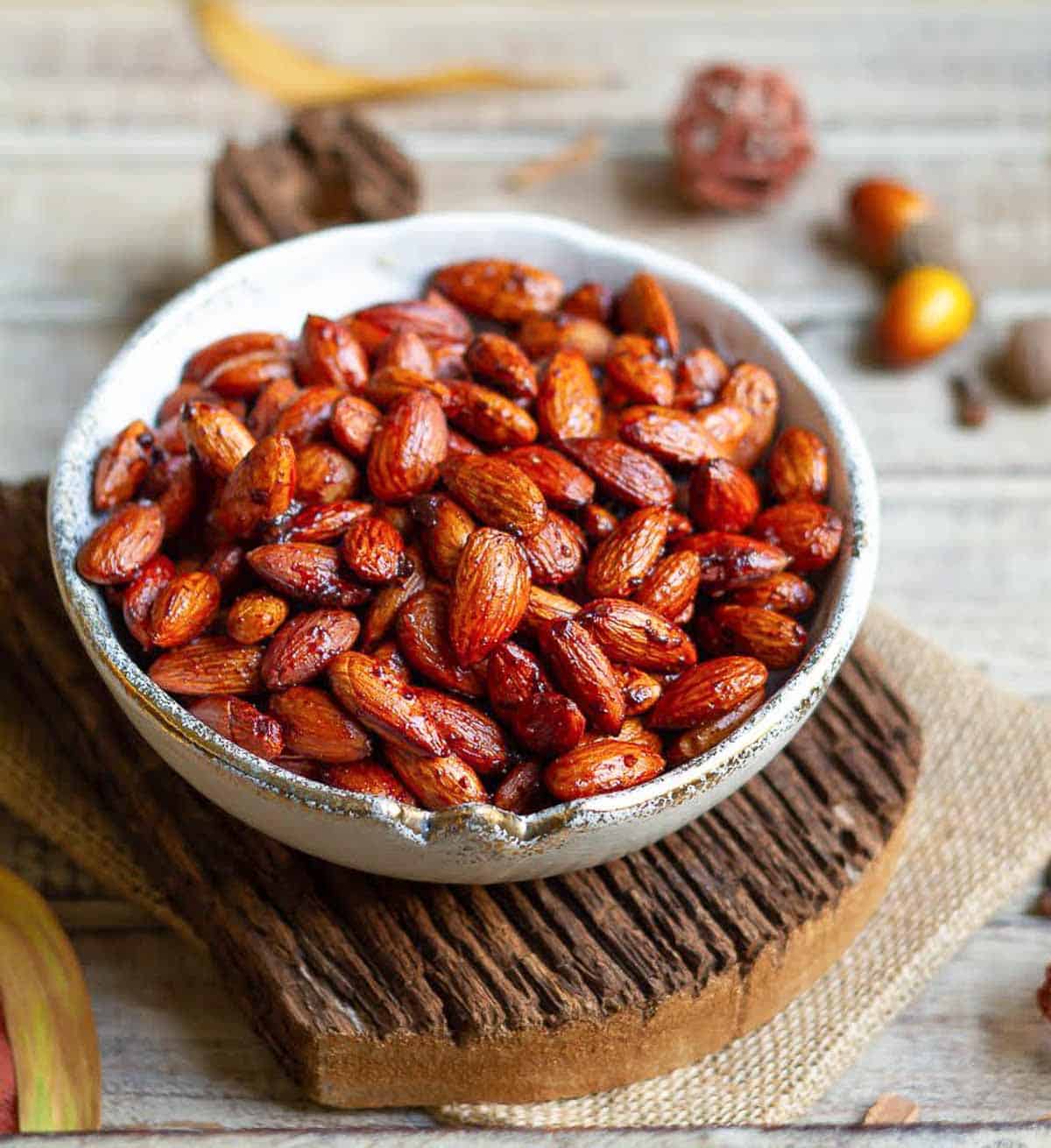 A bowl of spiced almonds on a wooden board with fall decor around.