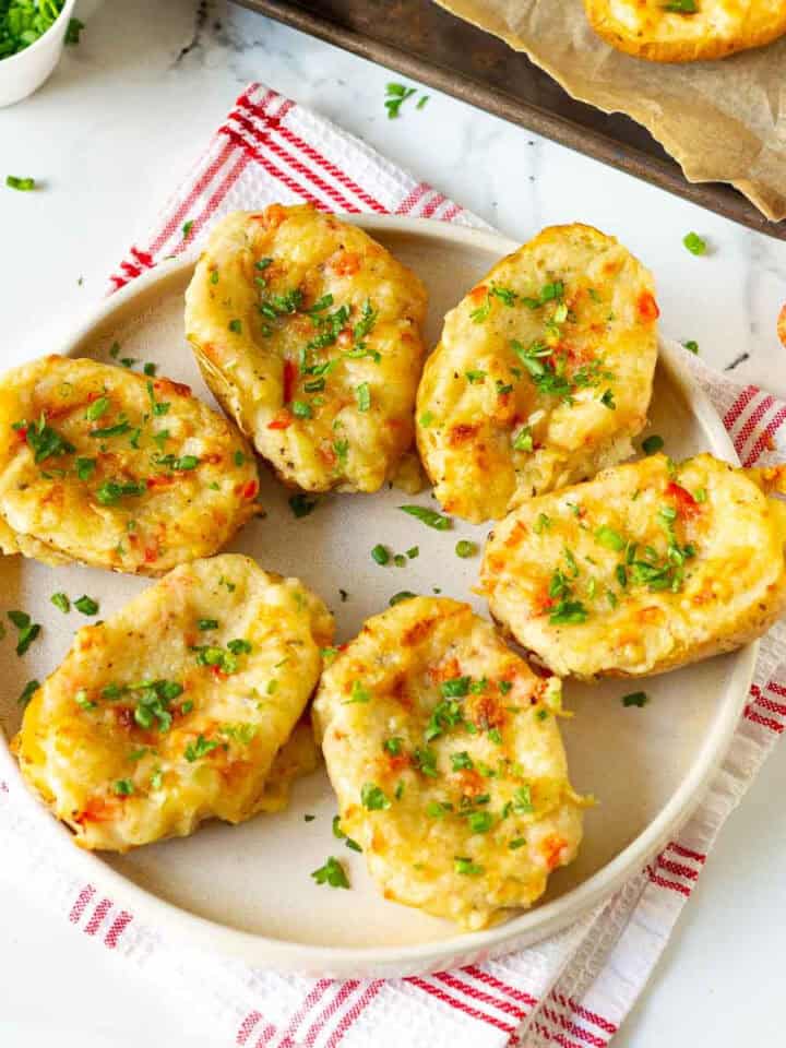 Loaded cheesy baked potatoes on a plate on a kitchen towel.