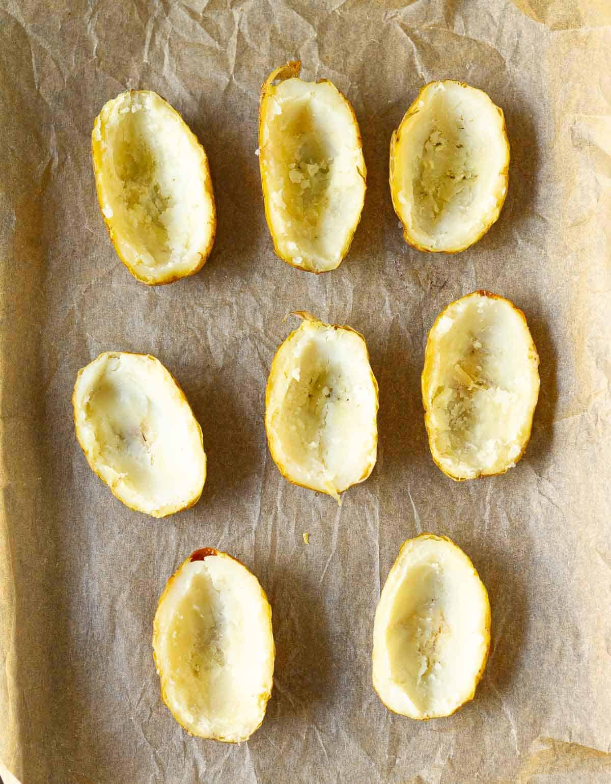 Hollowed out potato skins on a parchment-lined tray.