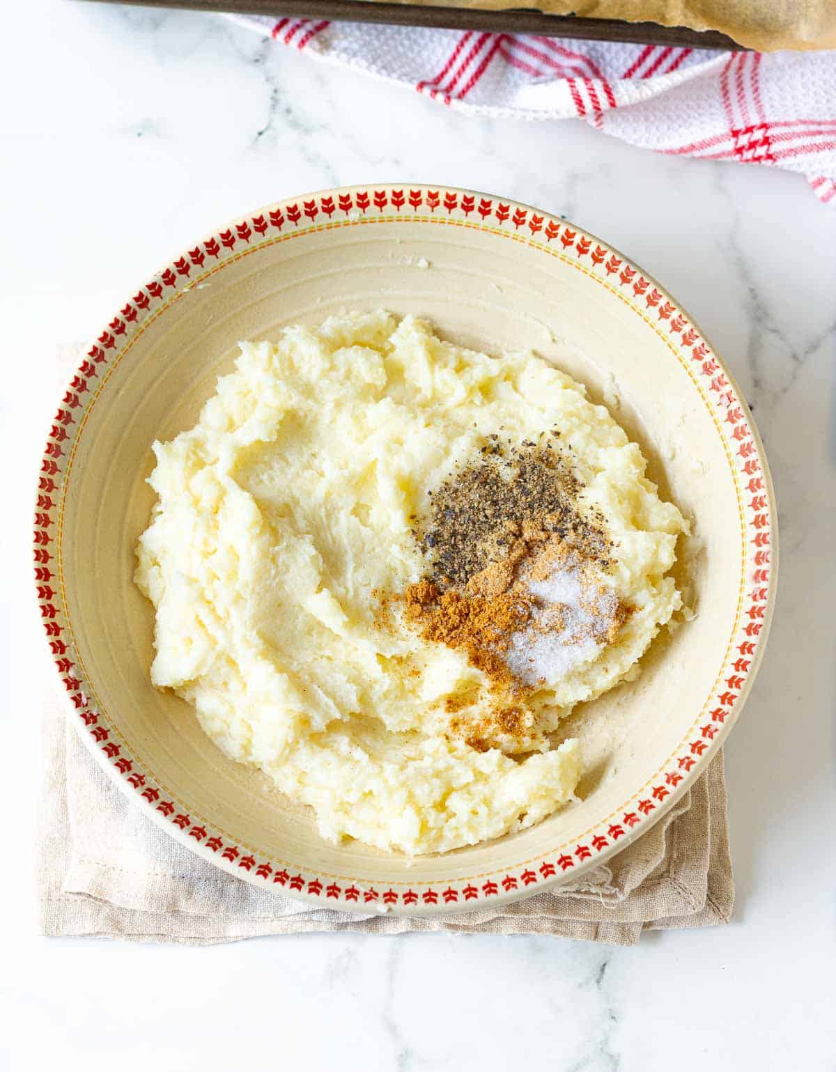Salt, garlic powder, onion powder, and pepper on mashed potatoes in a bowl.