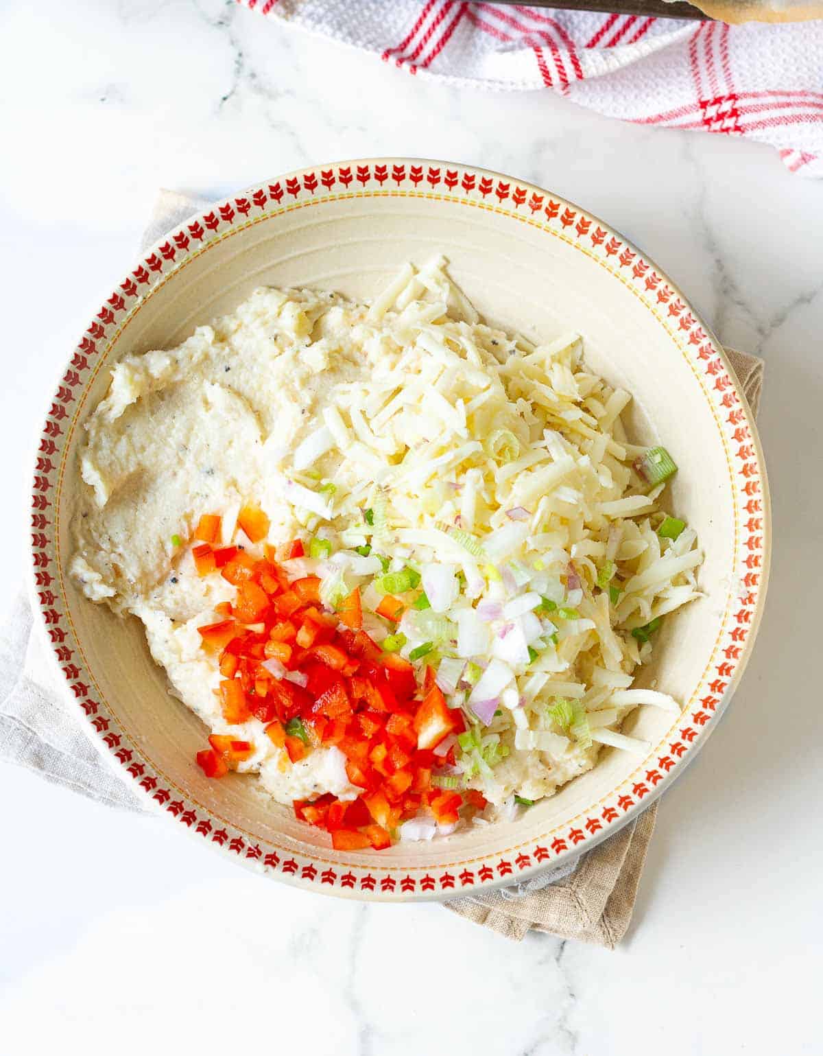 Shredded cheese, red bell pepper,and green onion on mashed potatoes in a bowl.