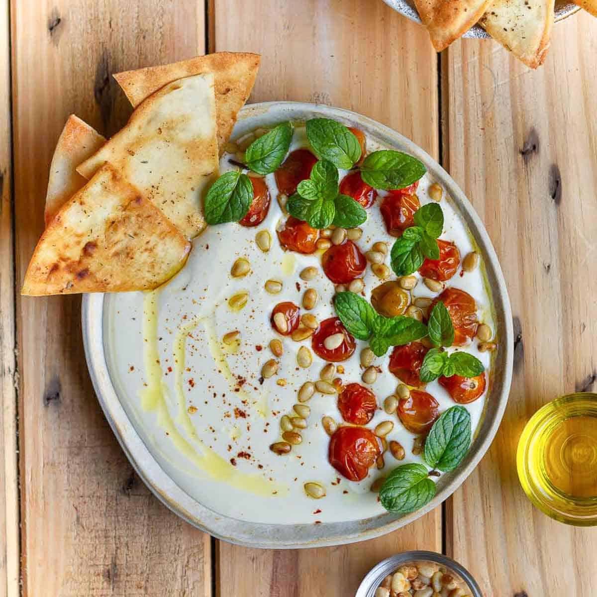 A bowl of dip with tomatoes, pinenuts and mint and tortilla chips.