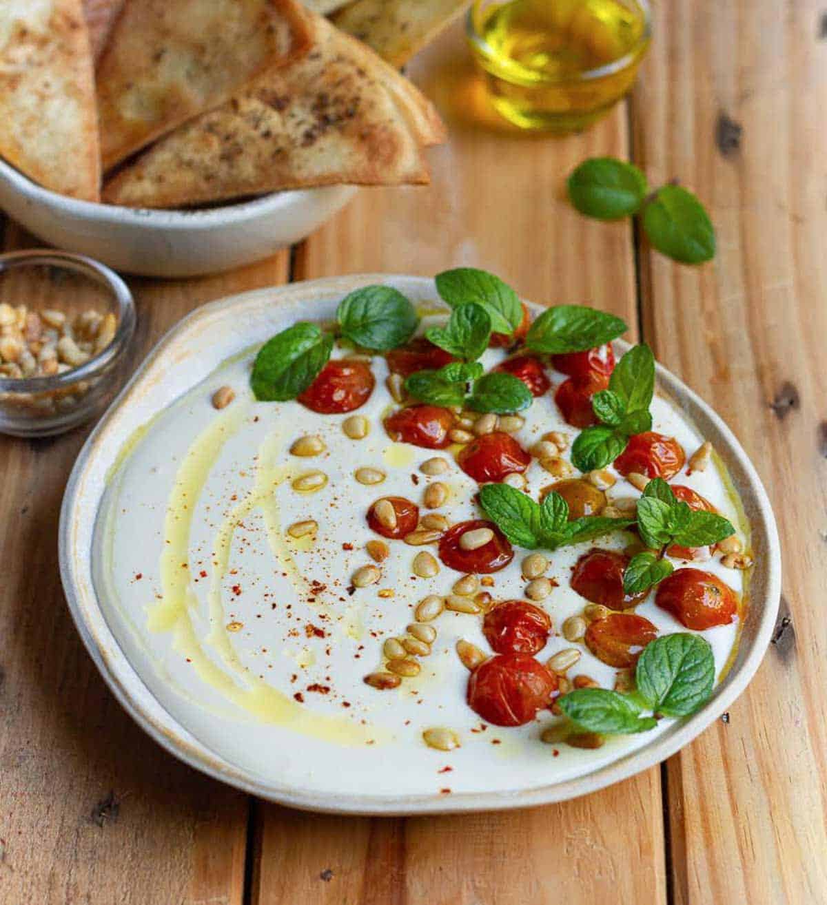 A bowl of dip on a wooden surface with ingredients around.