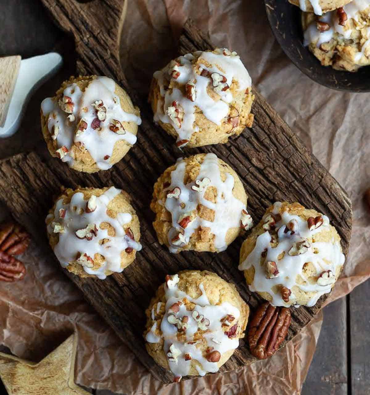 6 cookies with glaze and pecans on a wooden board.