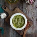 Pistachio pesto in a small white bowl with ingredients in the background.