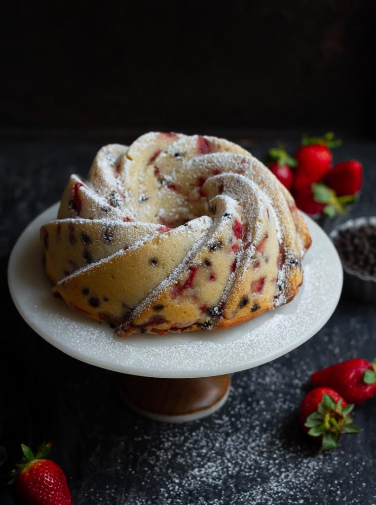 Strawberry Pound Cake on a cake stand with strawberries and chocolate chips in the background.