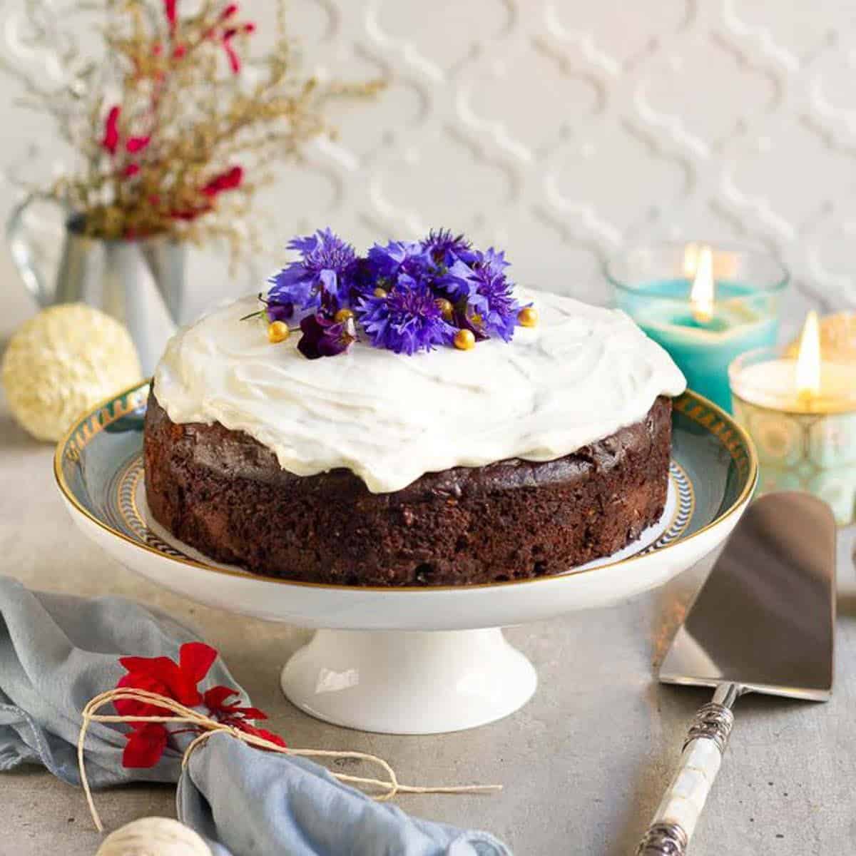 chocolate zucchini cake with cream cheese frosting and edible flowers on a cake stand.