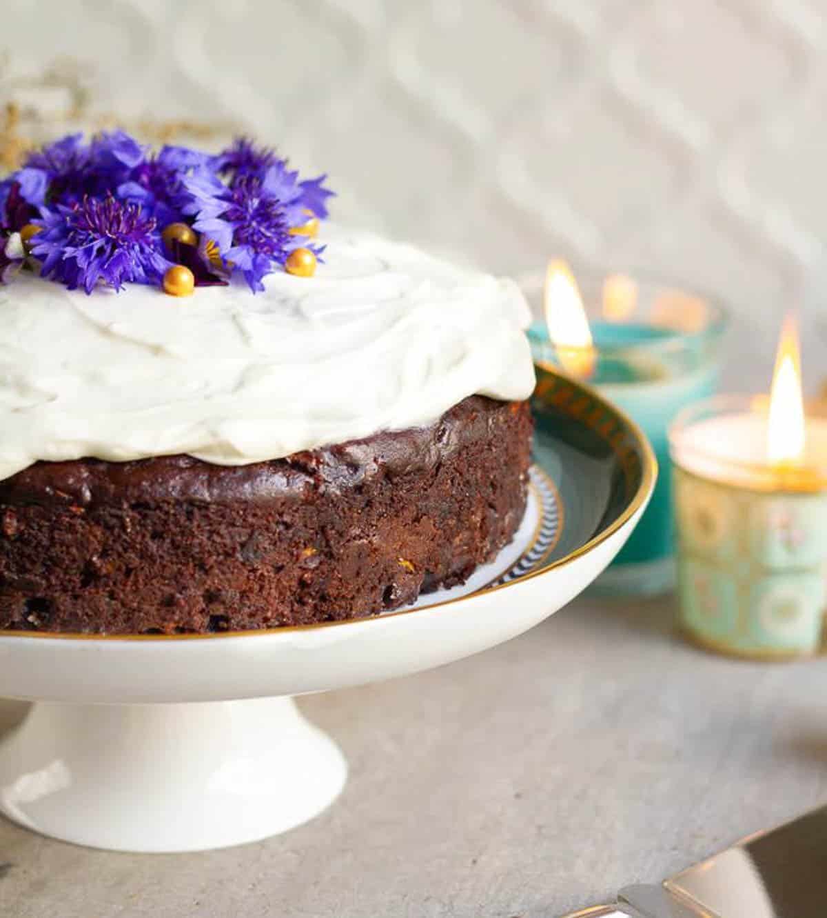 Moist chocolate zucchini cake with frosting on a cake stand.