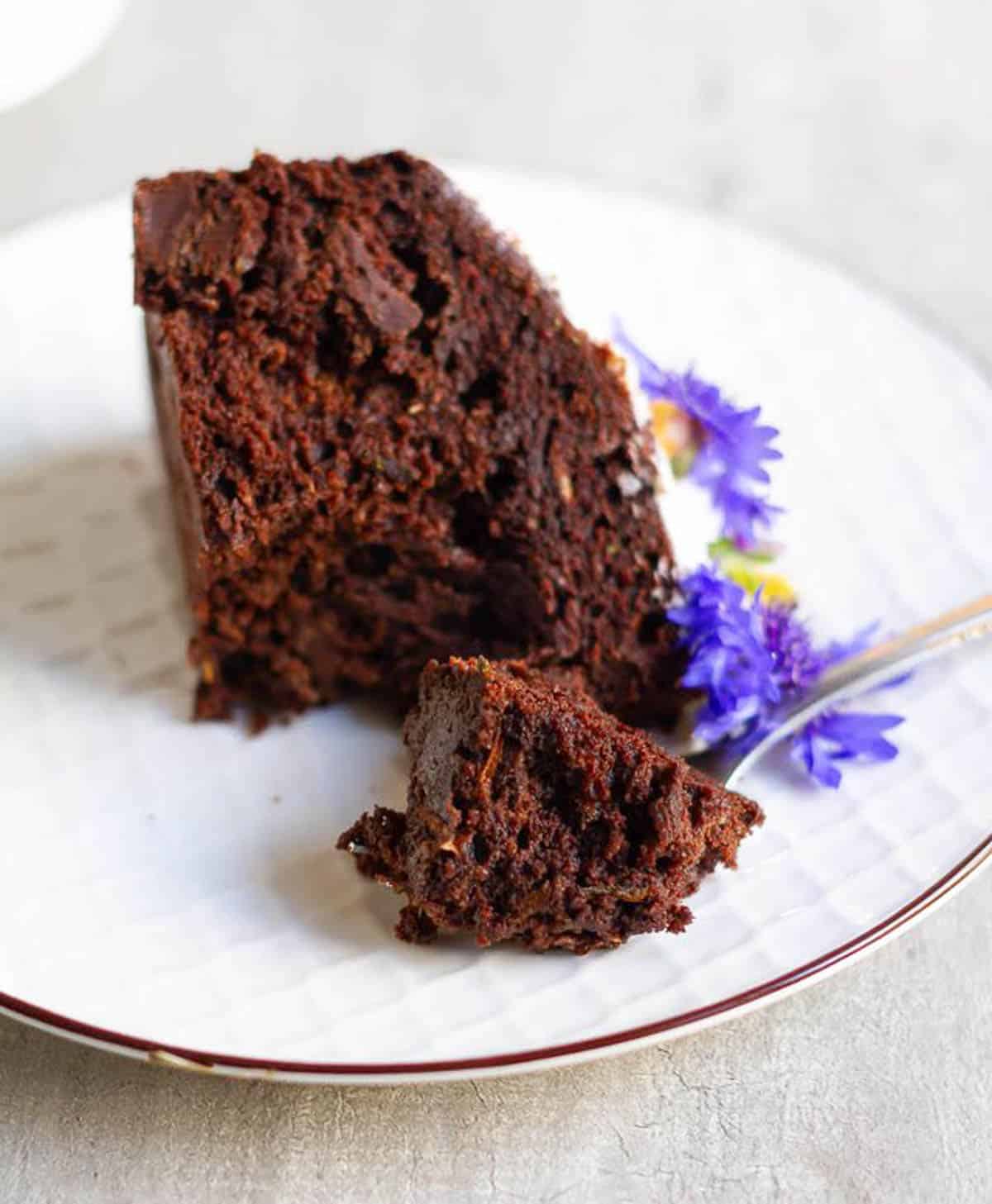A slice of chocolate cake on a plate with a bite taken out on a fork.