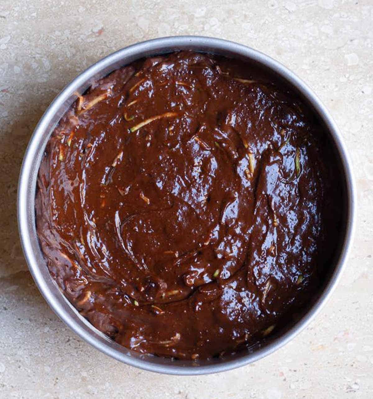 chocolate zucchini cake batter in a round cake pan.
