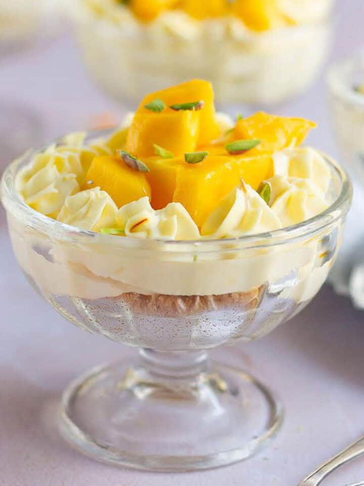 A dessert cup of no-bake mango cheesecake with fresh mangoes and pistachios.