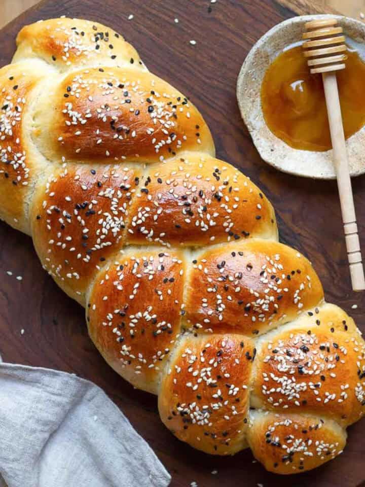 A braided loaf of bread with seeds on a wooden board with honey on the side.
