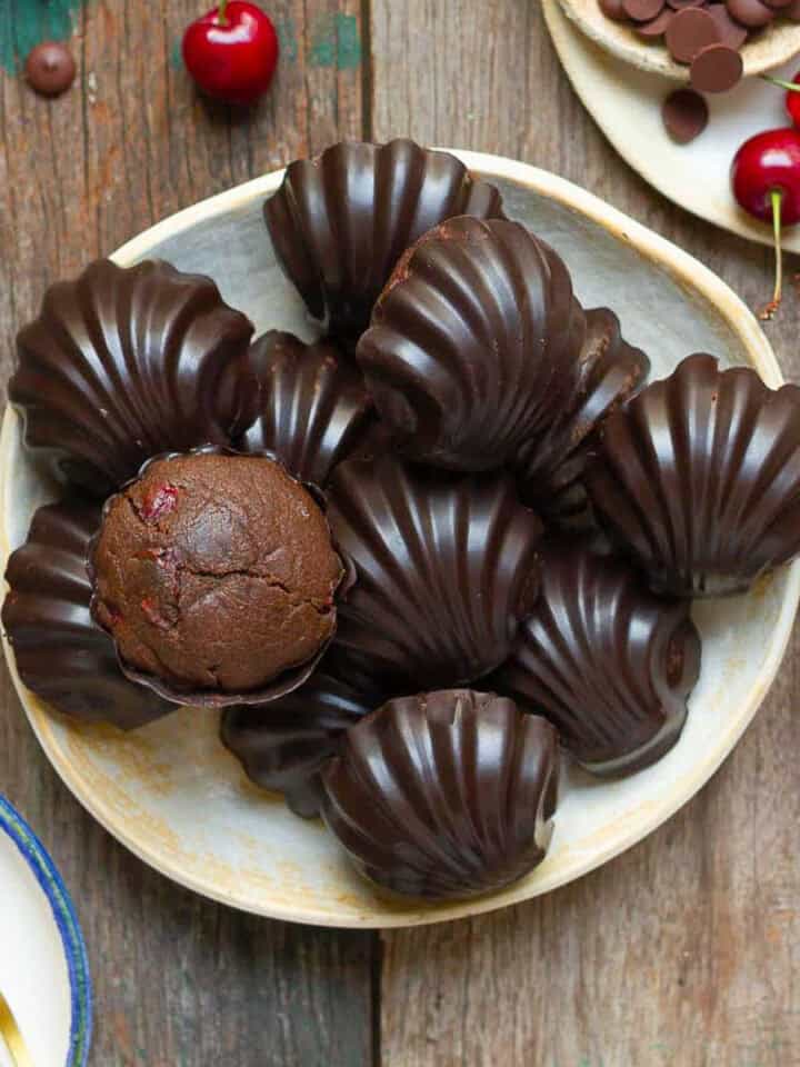 Chocolate cherry madeleines on a plate with ingredients in the background.