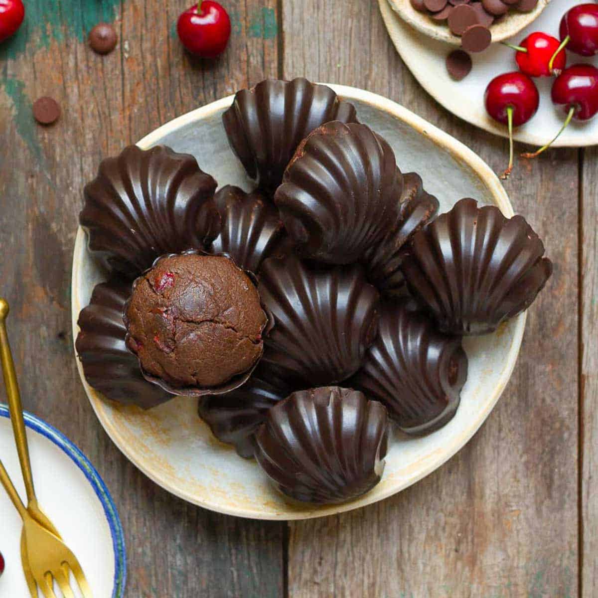 Chocolate cherry madeleines on a plate with ingredients in the background.