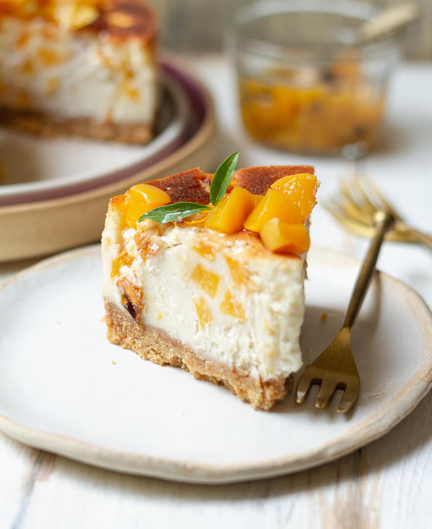 A slice of cheesecake with peaches on a small plate with a fork.