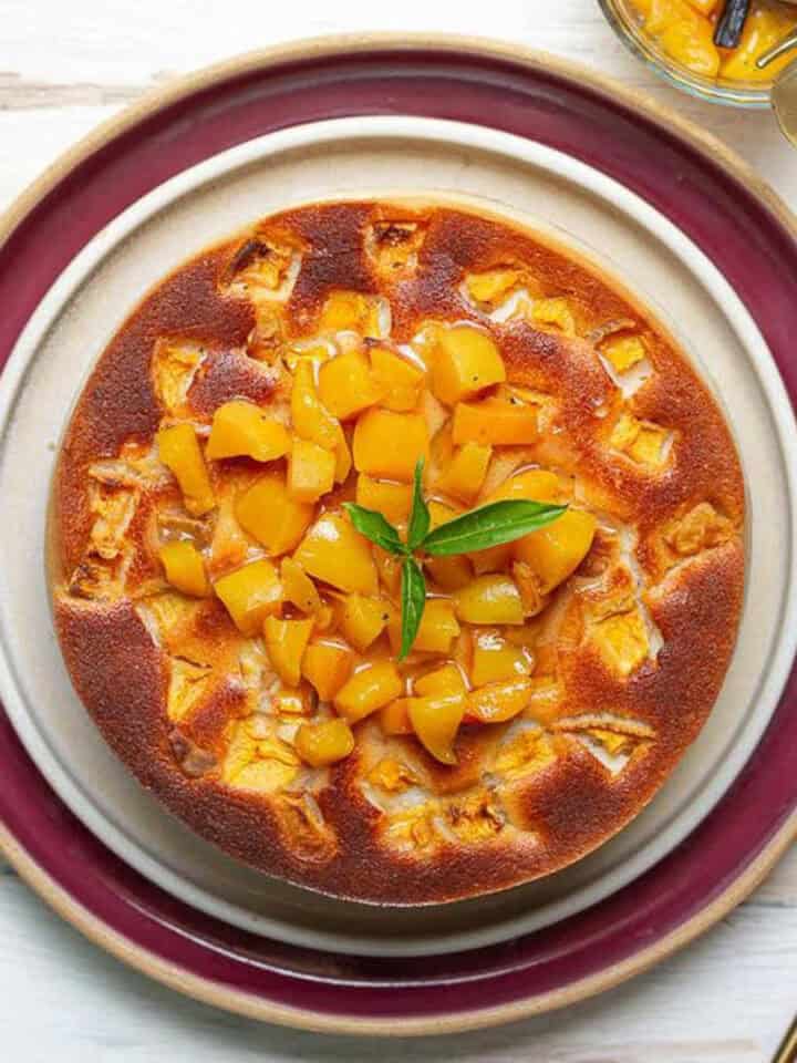 A peach cheesecake topped with compote and mint leaves on a platter.