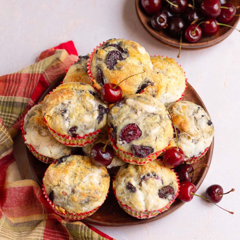 Cherry cheesecake muffins stacked on a plate with cherries around.