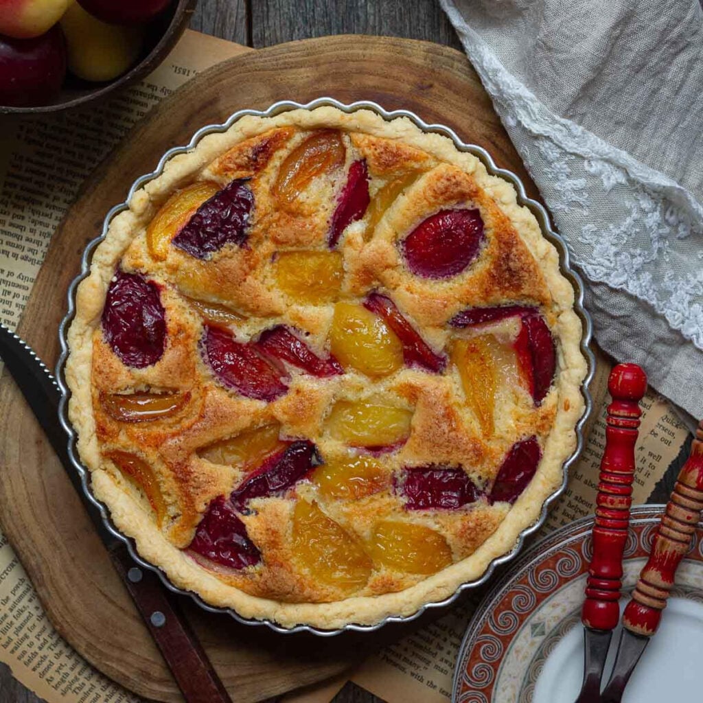Fruit tart on a wooden surface with 2 forks and fruits around.