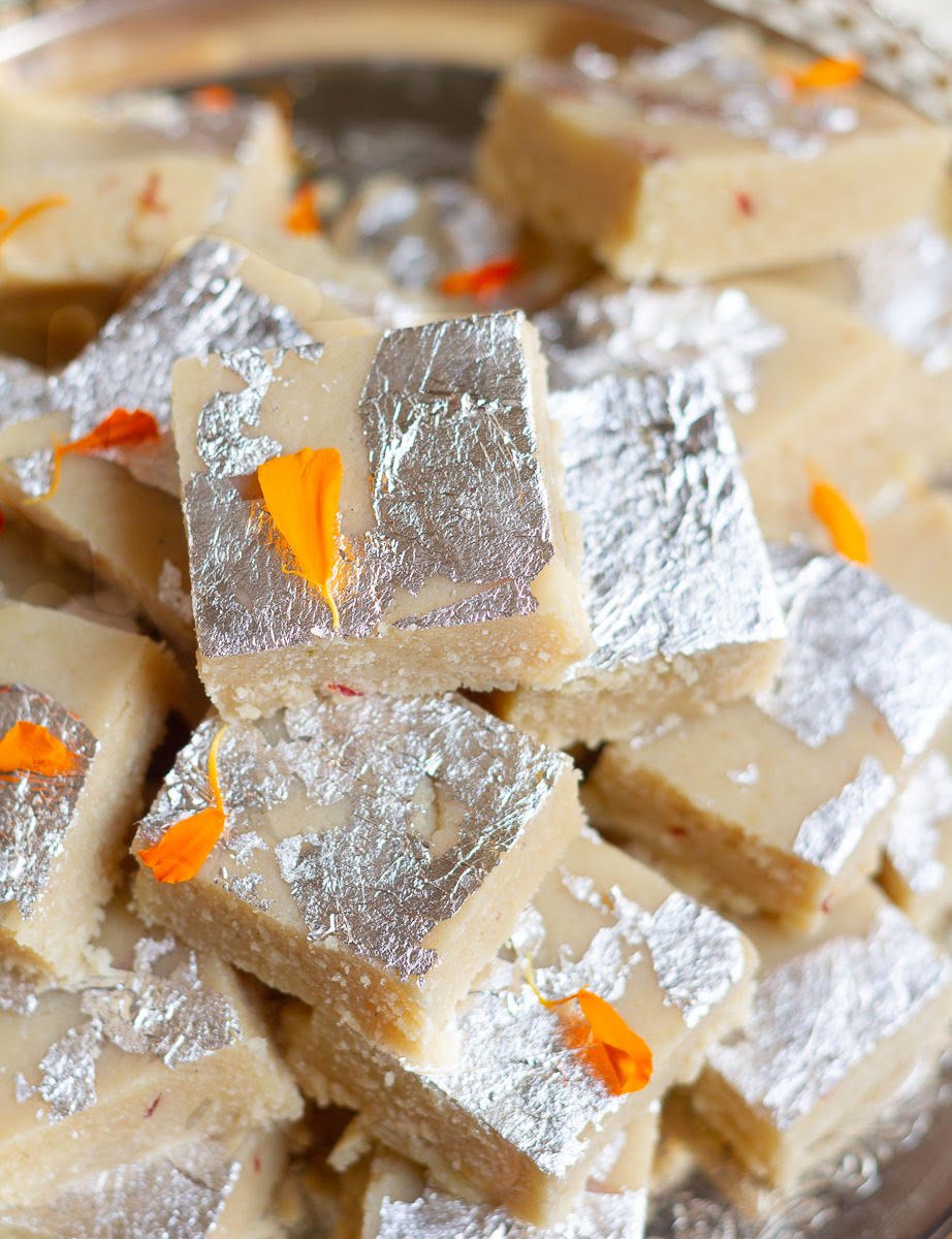 Almond burfi pieces garnished with silver leaf and marigold petals stacked up.