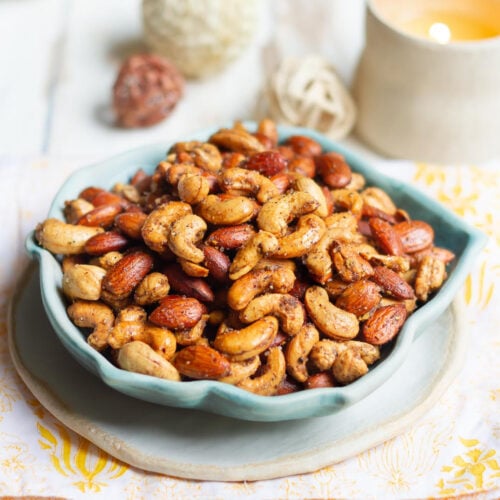 Roasted nuts in a blue bowl with a candle in the background.