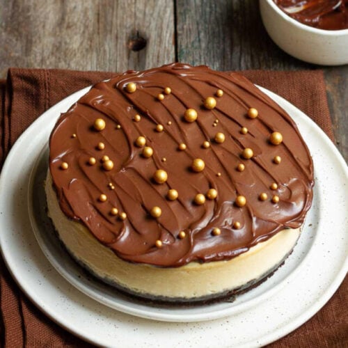 baileys cheesecake topped with chocolate ganache and golden sprinkles on a plate.