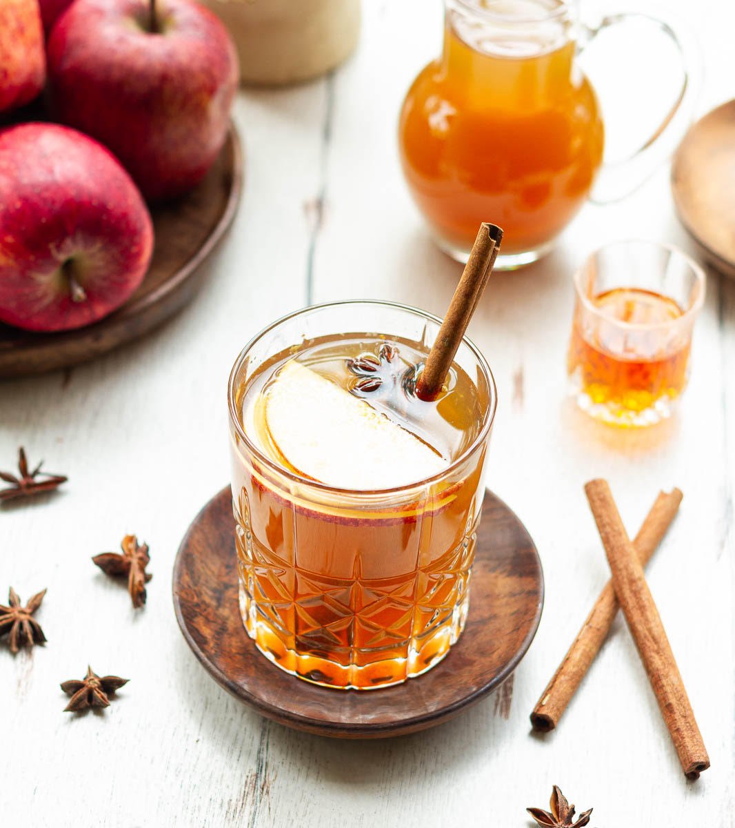 Apple Cider Hot Toddy in a glass with ingredients in the background.