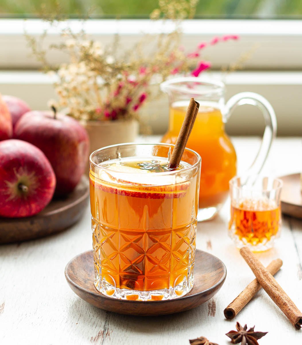 Apple Cider Hot Toddy in a glass garnished with cinnamon stick and apple slices.