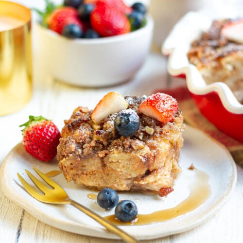 A slice of french toast casserole on a plate with berries and a fork.