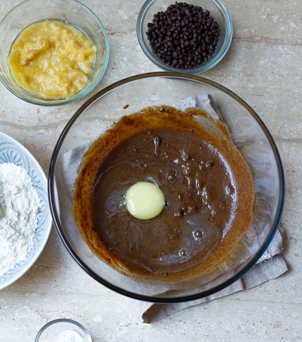 Butter, muscovado sugar, egg and vanilla extract in a big bowl. Bowls with flour, chocolate chips, mashed banana around the big bowl