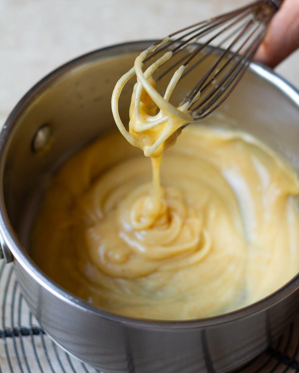 Brown butter icing in a small saucepan with a small whisk