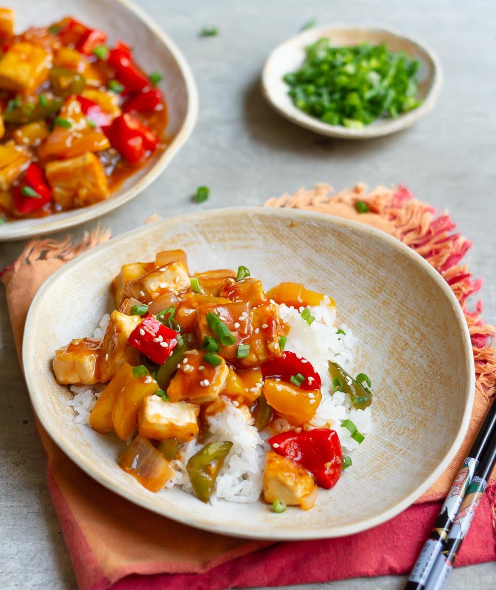 Crispy Tofu With Sweet and Sour Sauce served atop sticky rice, garnished with spring onions and sesame seeds