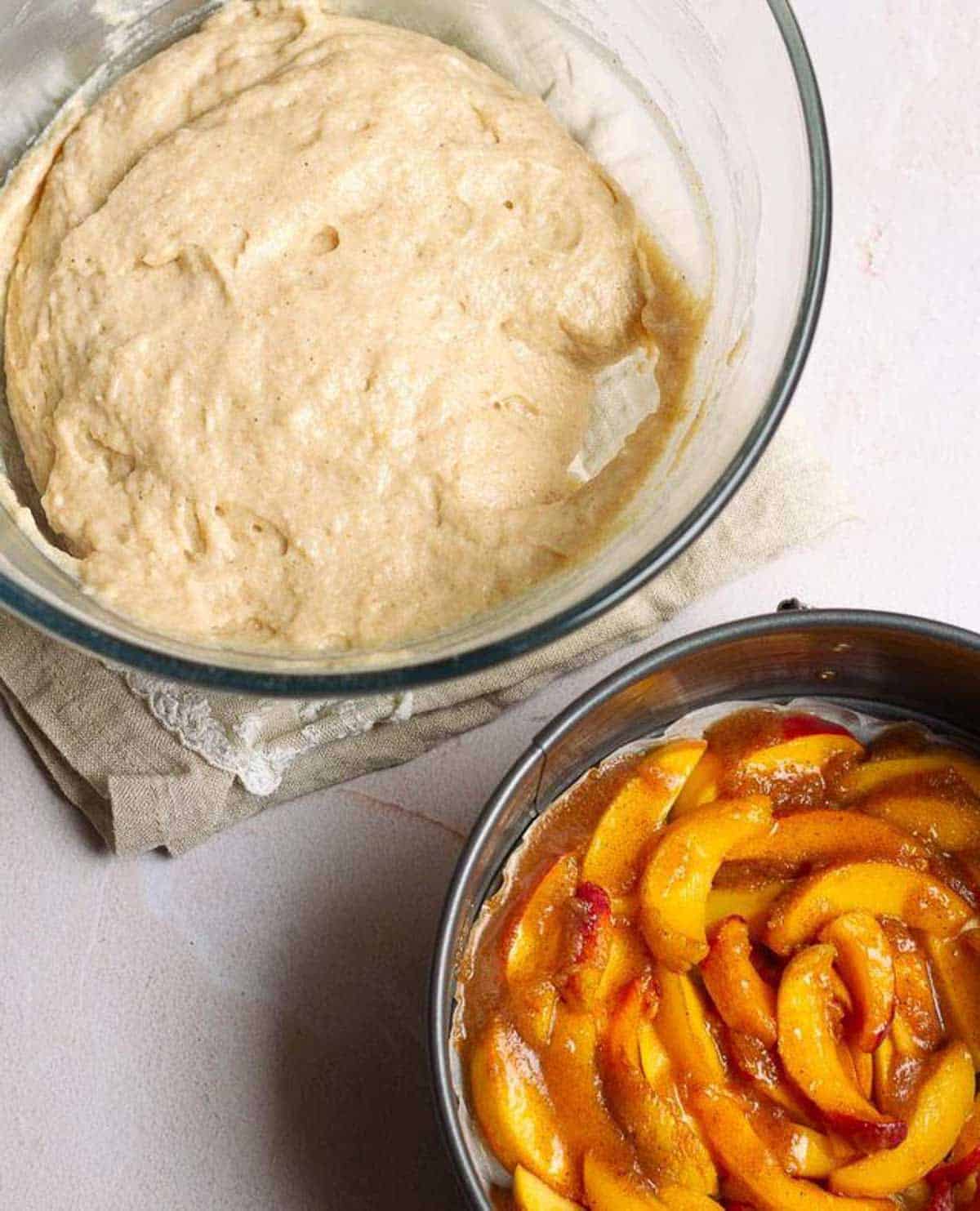 Peaches in a cake pan and cake batter in a bowl on the side.