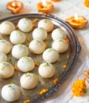 Paneer laddus on a silver tray with diyas and marigold flowers.