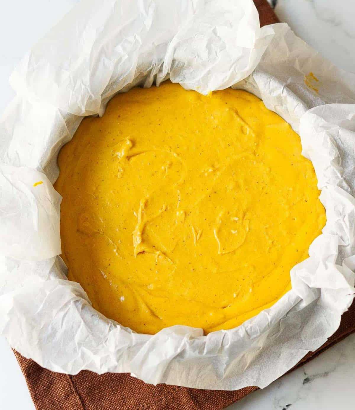 pumpkin cheesecake batter in a parchment paper lined cake pan.