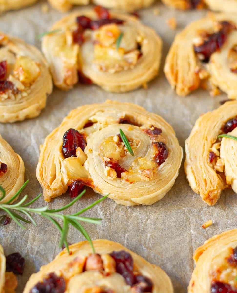 Cranberry Brie Puff Pastry Bites on parchment paper with fresh rosemary sprigs.
