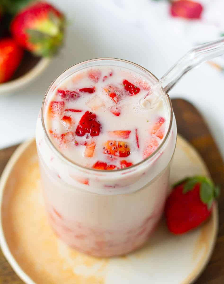 Strawberry milk in a glass with a glass straw on a small plate.