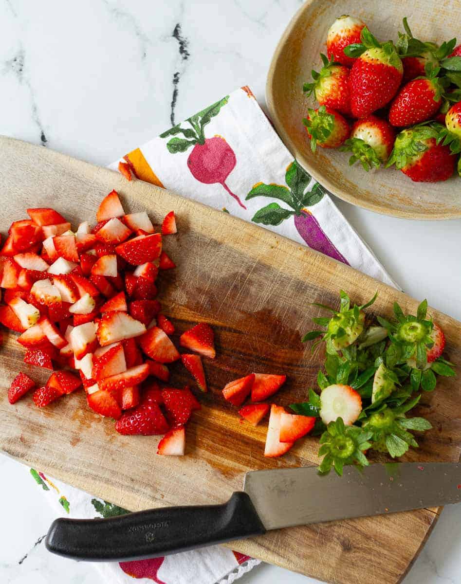 chopped strawberries on a wooden chopping board.