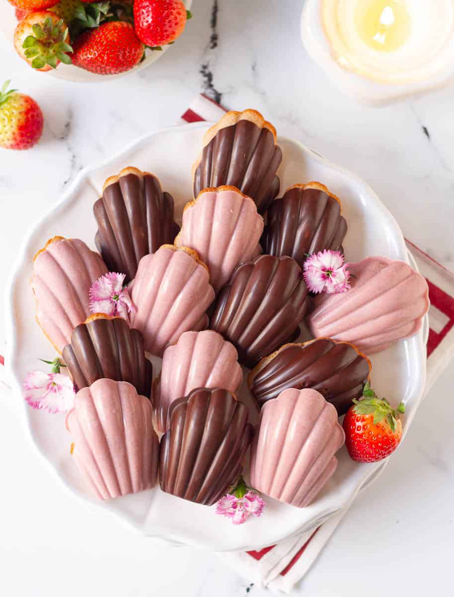 strawberry madeleines on a white serving plate with fresh strawberries and edible flowers.