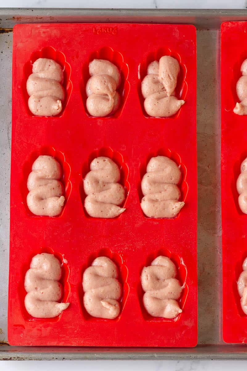 Piped batter in a red silicone madeleine mold.