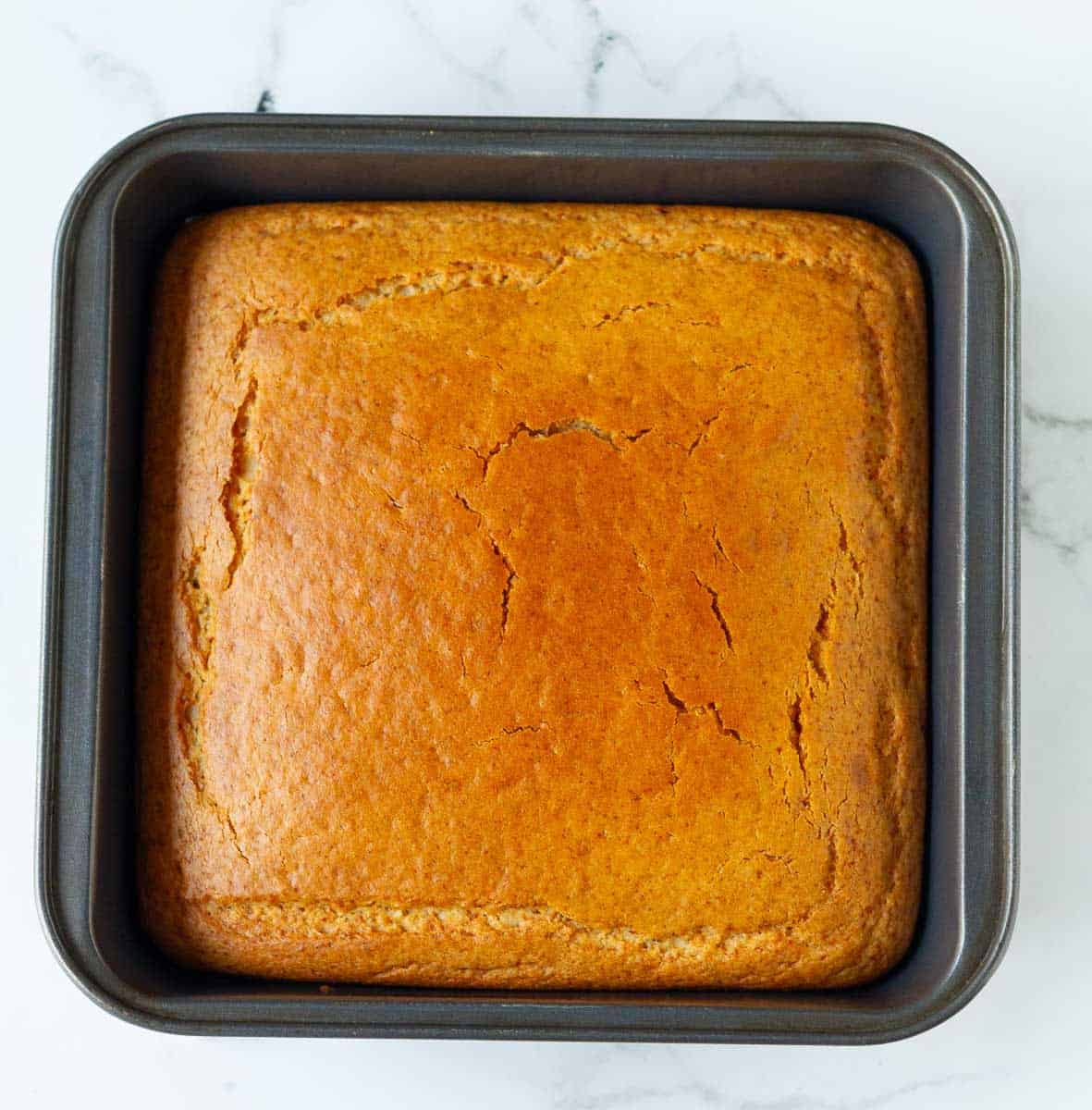 Baked cake for making strawberry poke cake in a square metal cake pan.