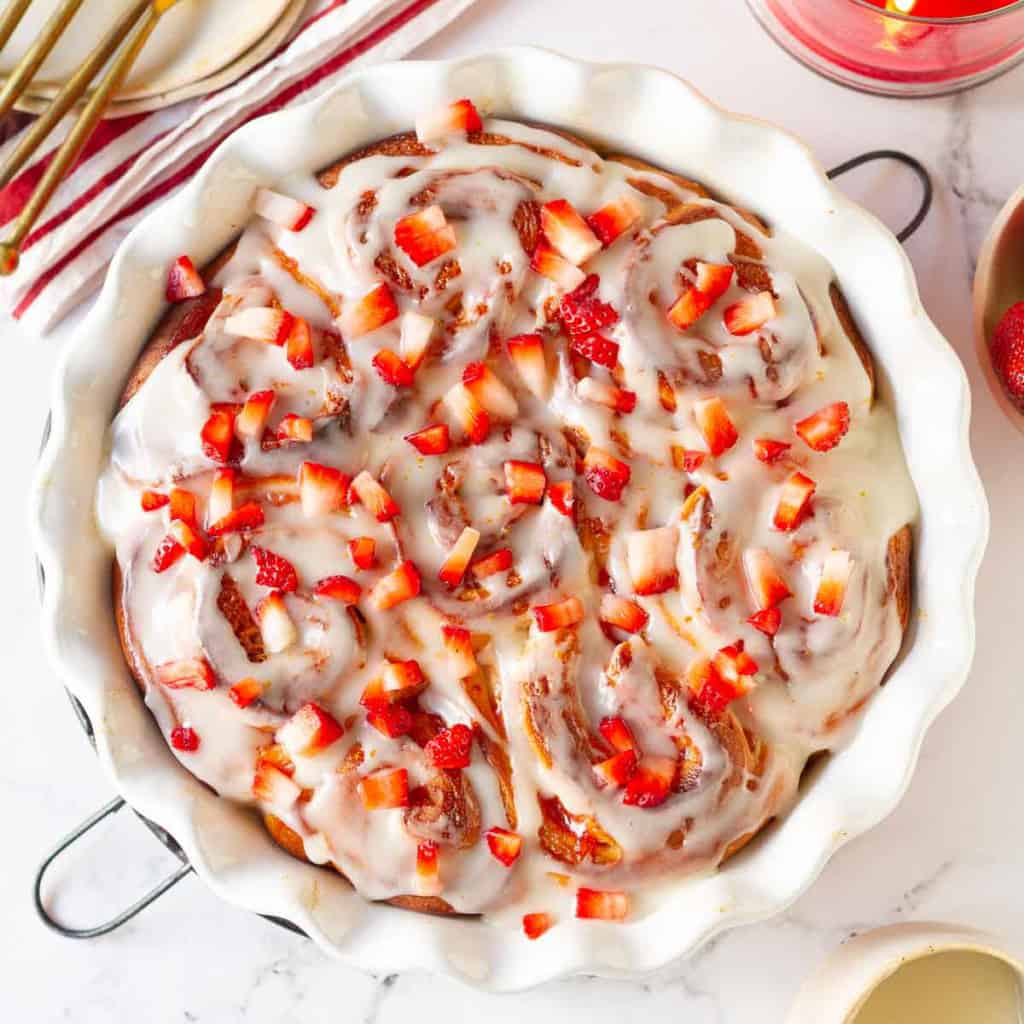 Strawberry rolls in a round baking dish with cream cheese glaze.