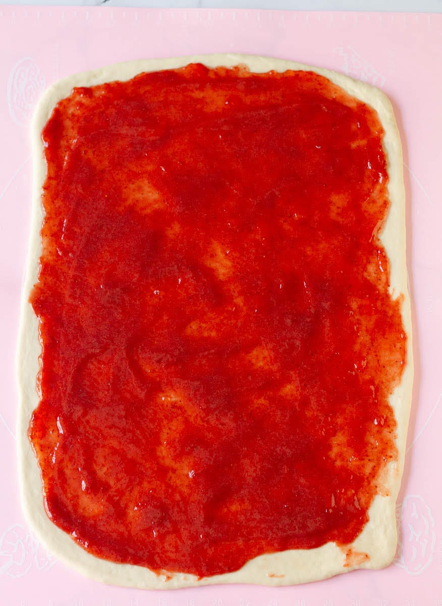 strawberry jam spread over the rolled out dough