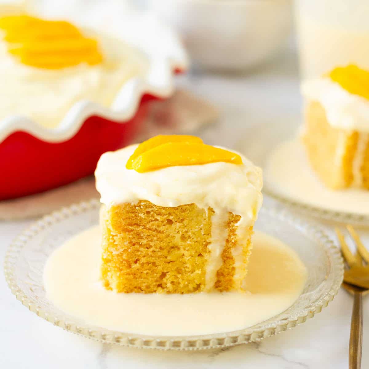 A slice of mango tres leches cake on a plate with a fork on the side.