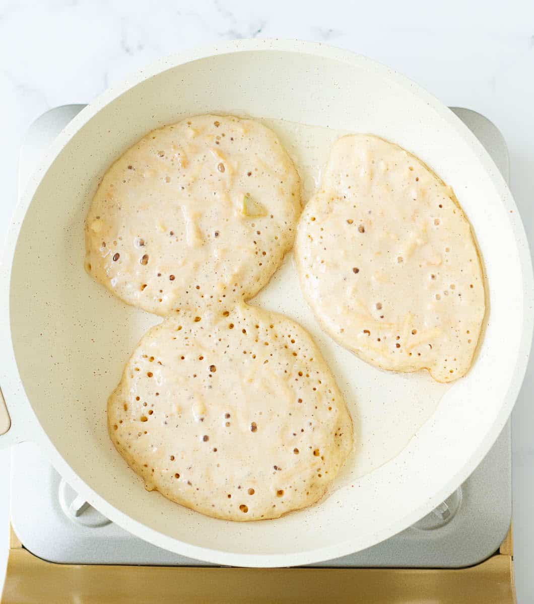 cooking 3 pancakes in a white skillet.