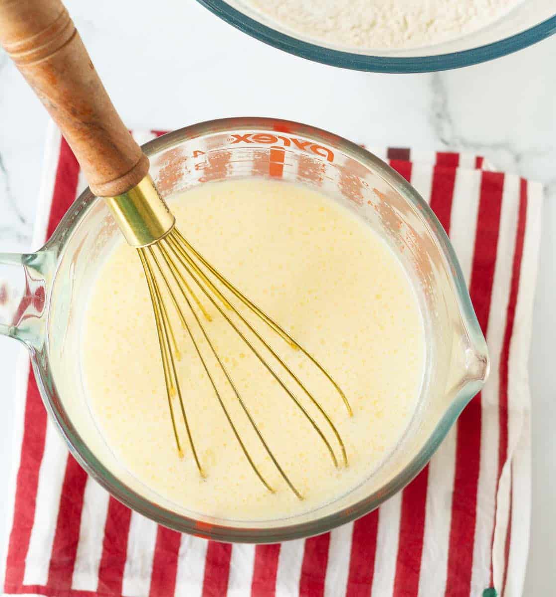 mixing wet ingredients for apple pancakes in a glass measuring cup.