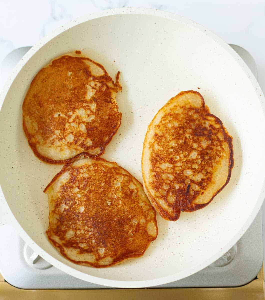 cooked apple pancakes in a white skillet.