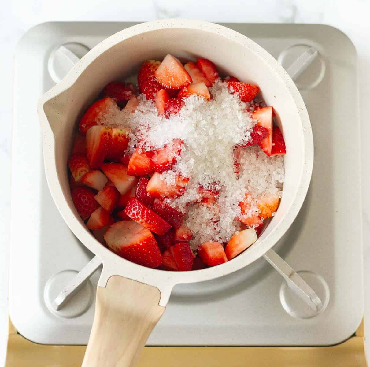 chopped strawberries and sugar in a white saucepan.