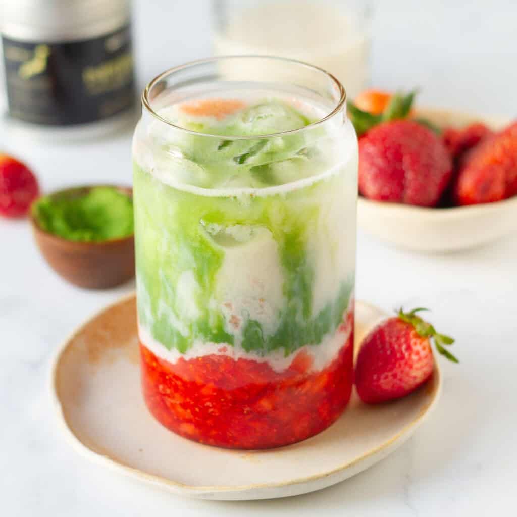 matcha strawberry latte in a glass placed on a plate with ingredients in the background.