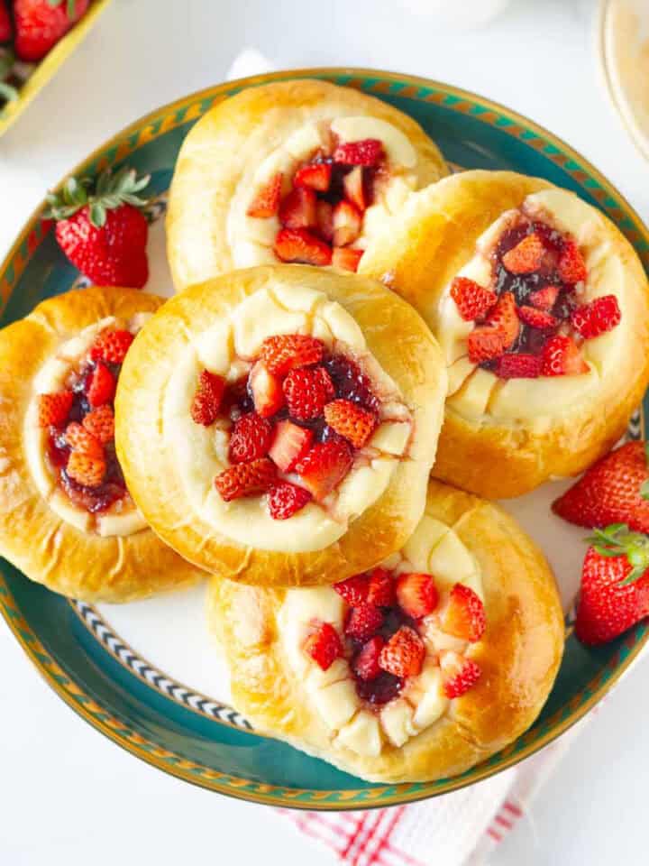 Strawberry cream cheese rolls stacked on a cake stand with strawberries on the side.